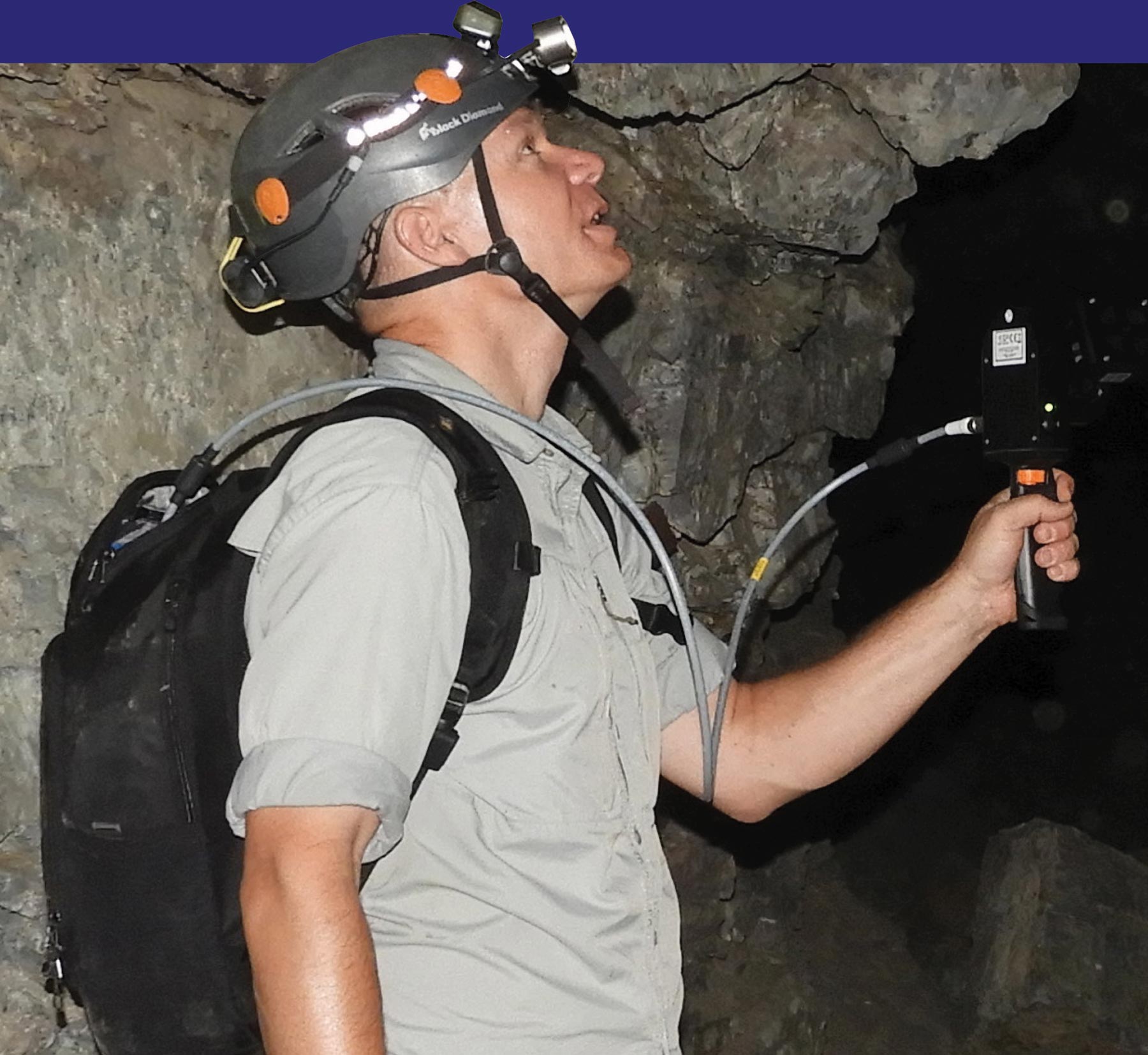 man walking through cave with a helmet, a backpack, and a video camera