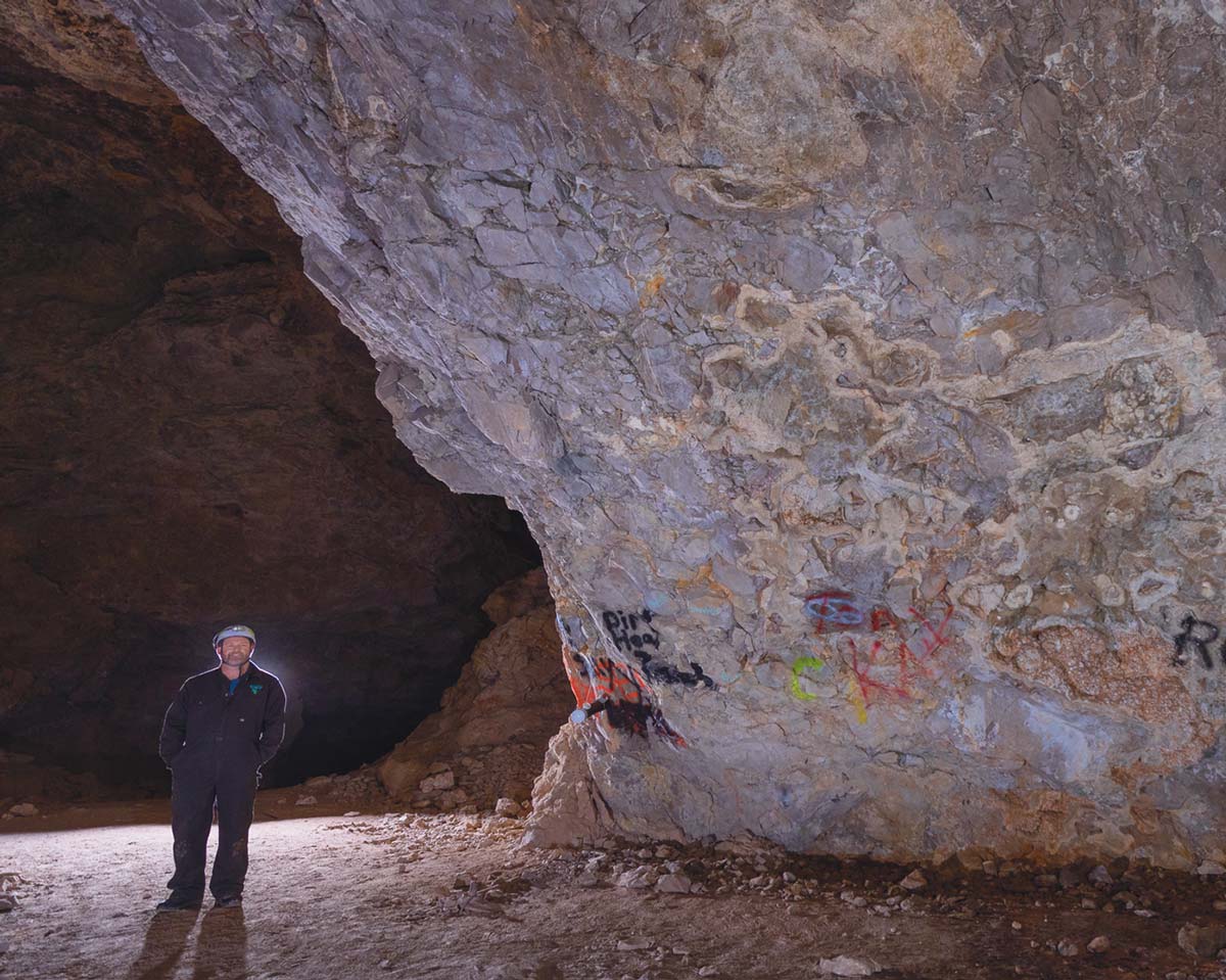 Person standing next a cave wall with graffiti