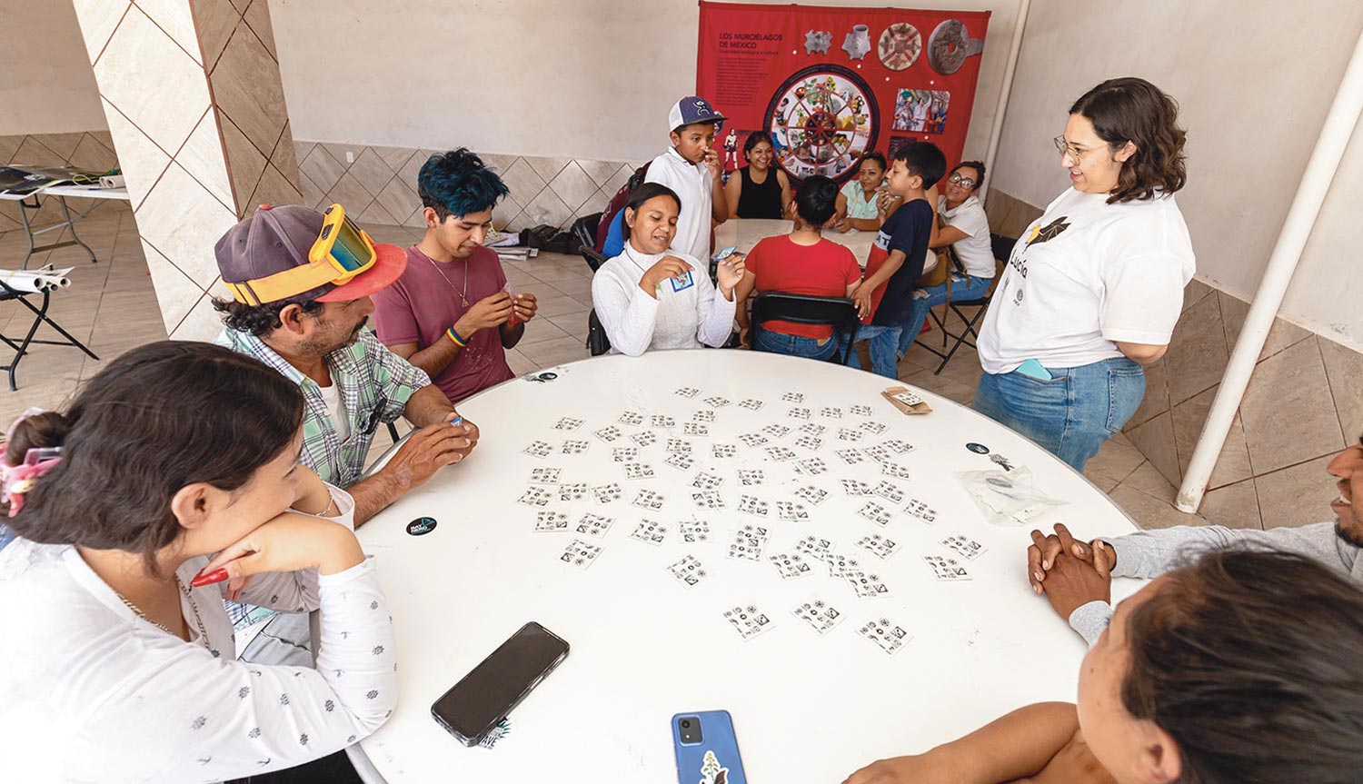 two groups of people sit at circular tables and engage in an educational activity