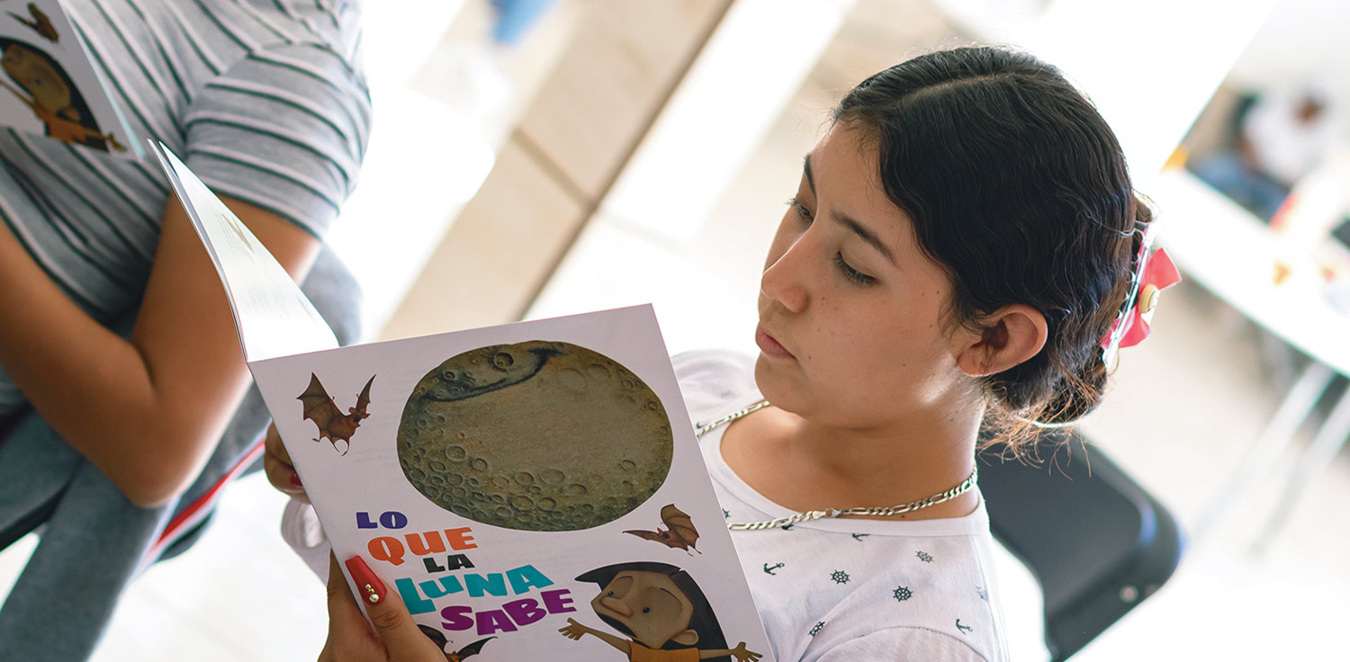 a young woman looking through the book “Lo que la Luna Sabe,” (“What Luna knows”)