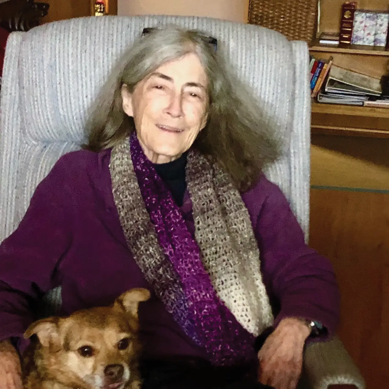 Merrill How Leavitt smiling and seated with dog in chair