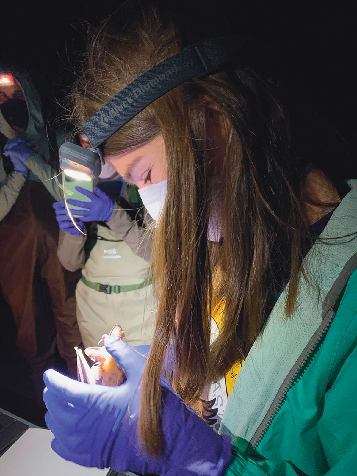 girl wearing mask and headlamp while holding a small bat