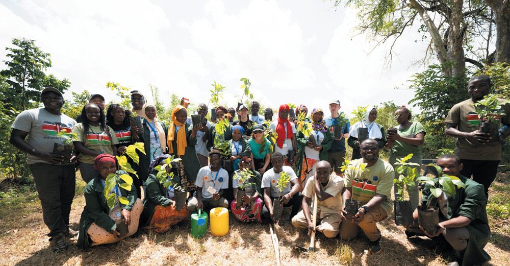 A group of diverse people holding tree saplings in a natural outdoor setting.