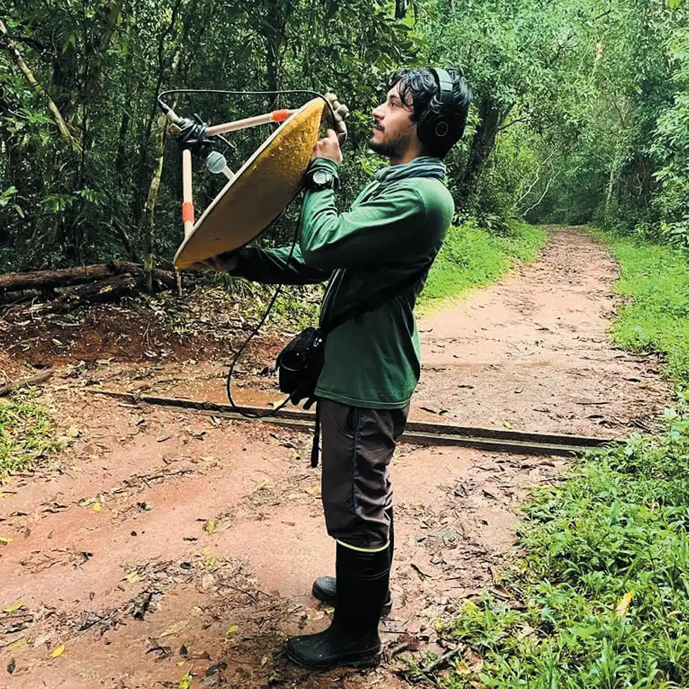 Person using a parabolic microphone in a forested area.