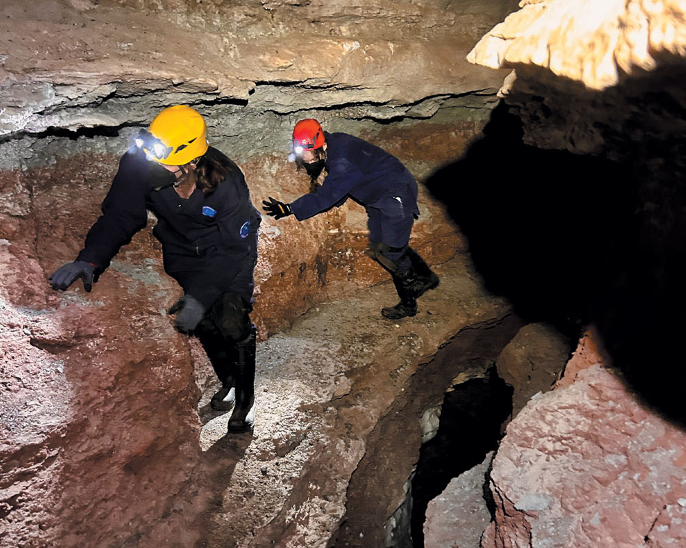 Two people exploring a cave with headlamps and protective gear.