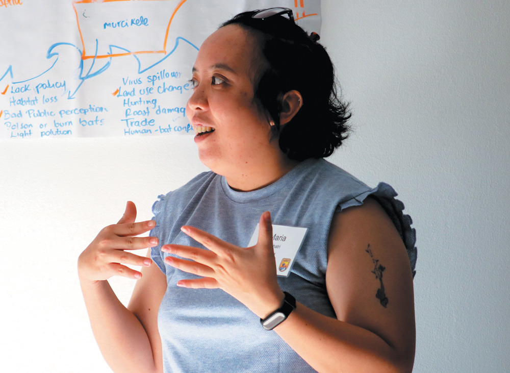 A person gesturing while speaking in front of a whiteboard filled with handwritten notes.