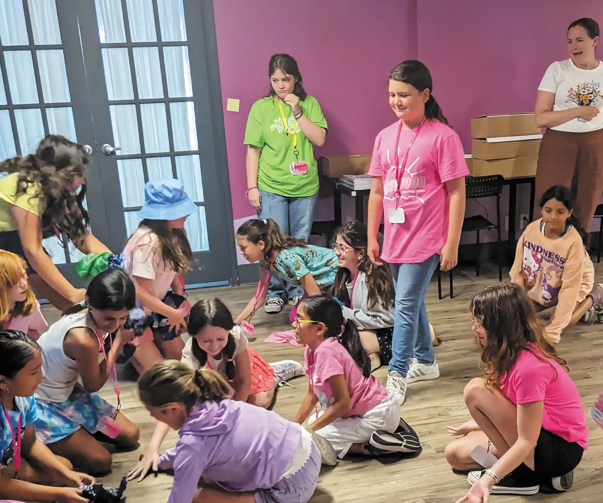 A group of campers from Girlstart are gathered in a room with pink walls and a wooden floor, engaged in BCI’s Batnado activity.