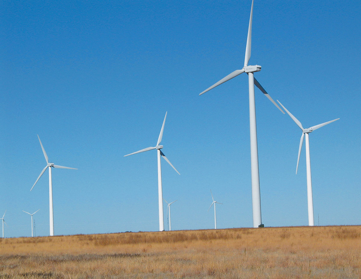 Several large, white wind turbines stand across a dry, golden grassy hill under a clear blue sky.
