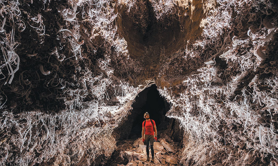 A researcher with a headlamp standing inside a cavern filled with intricate white gypsum formations.