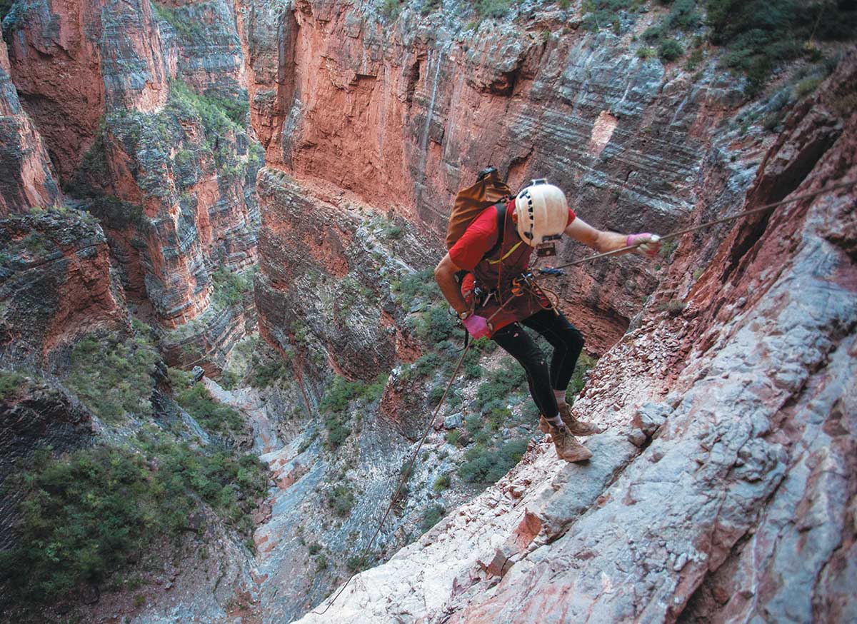 A researcher rappelling down a steep, rocky cliffside near a deep canyon.