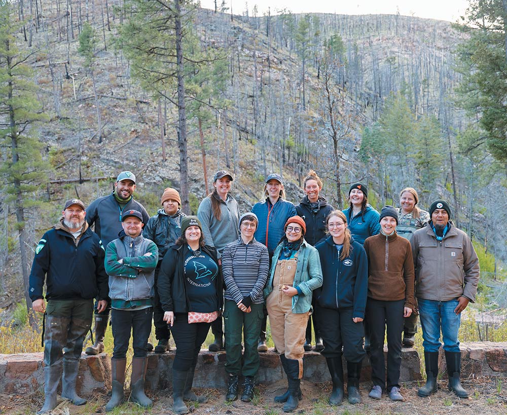 Group of researchers and conservationists posing outdoors in front of a wooded hillside.